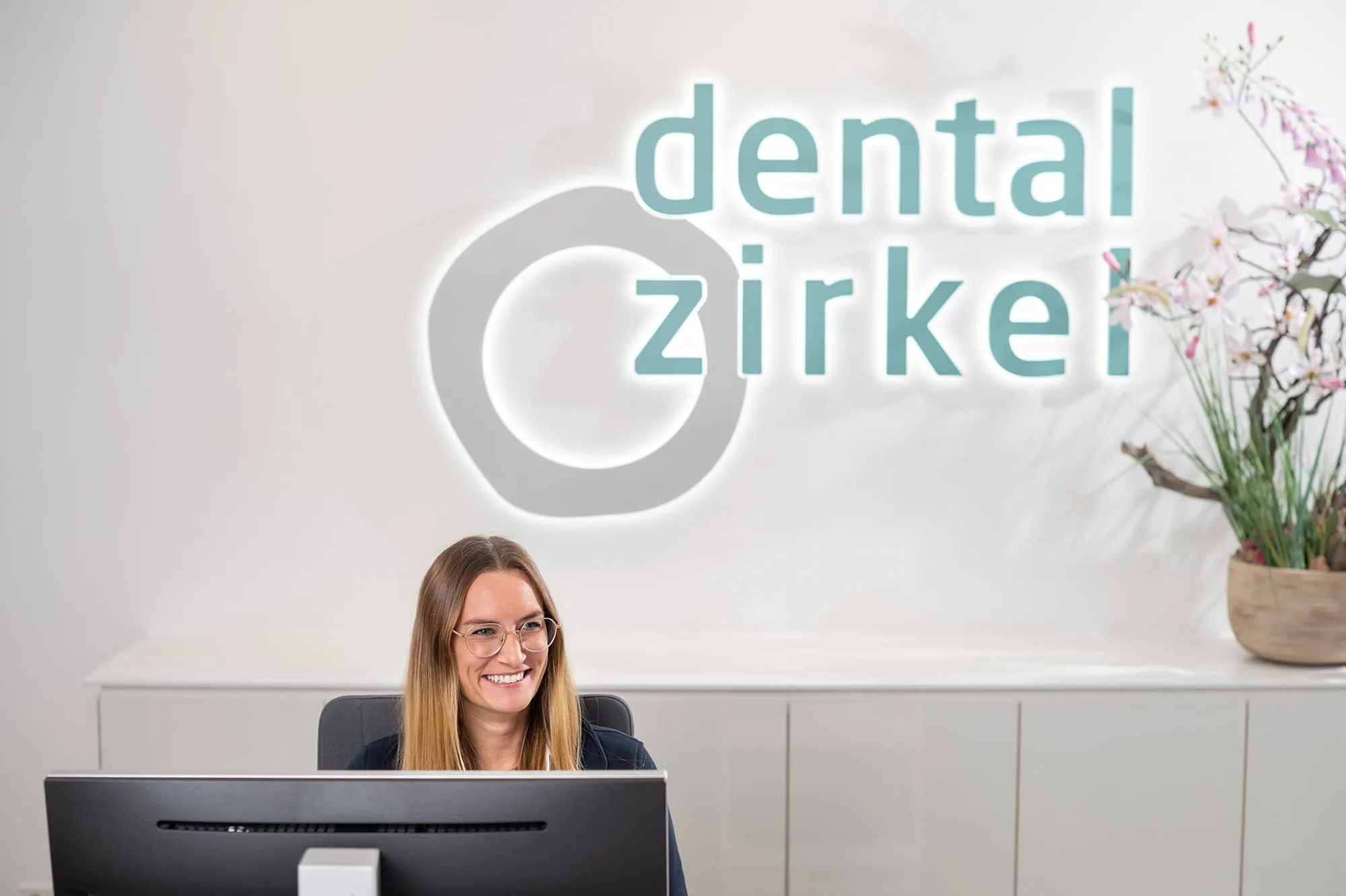 Freundliches Empfangsteam in der Praxis Dentalzirkel: Eine lächelnde Mitarbeiterin begrüßt die Patienten im Empfangsbereich